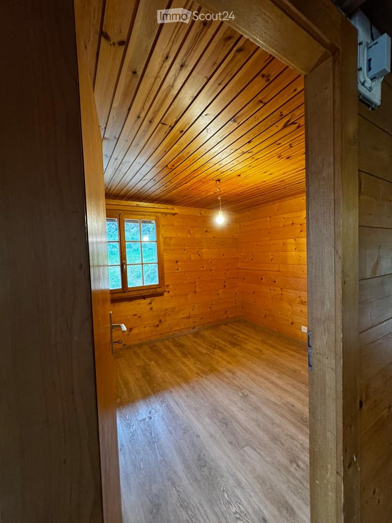 empty room, wooden walls, wooden floor, small window, light hanging from ceiling
