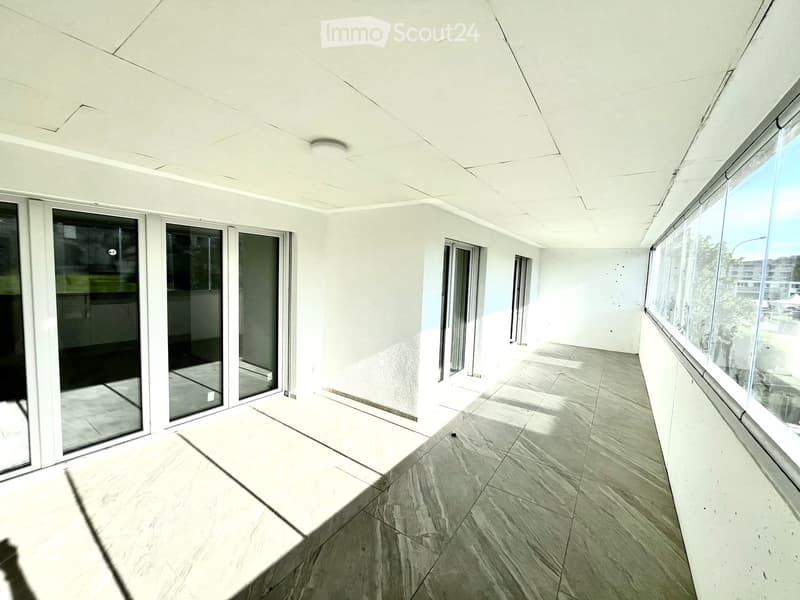 Empty room with white walls, large windows, tiled floor, and a ceiling light