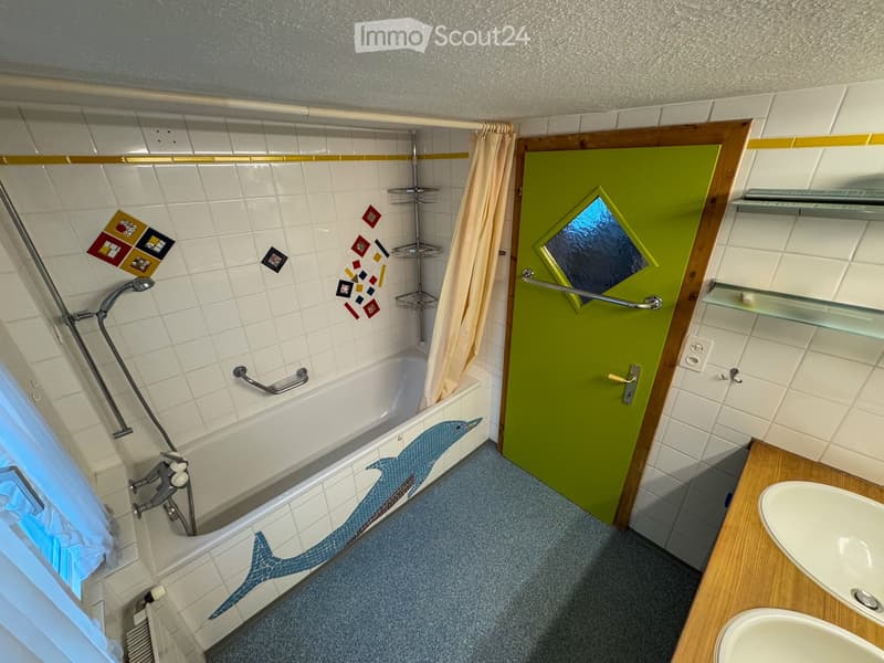 Bathroom with white tiles, bathtub with dolphin design, green door, two sinks, shower head, and a towel rack.