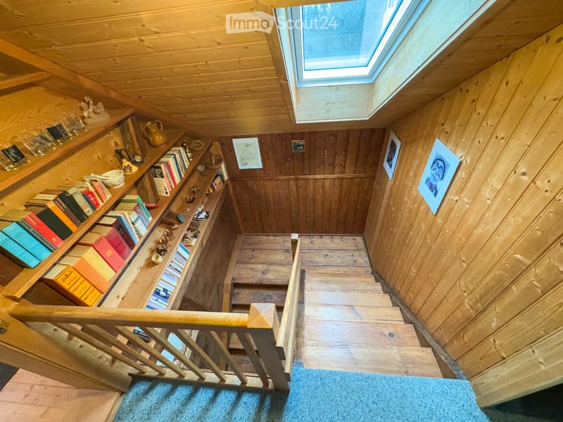 wooden staircase with wooden handrail, wooden steps, wooden wall, wooden ceiling, skylight, wooden shelf with books, picture frames on the wall