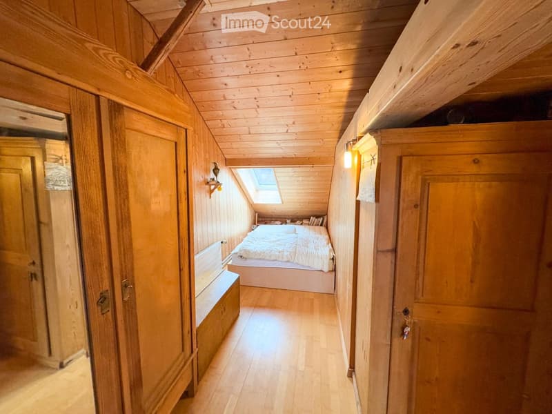Small bedroom with wooden walls and floor, bed, bench, wooden cabinet, skylight