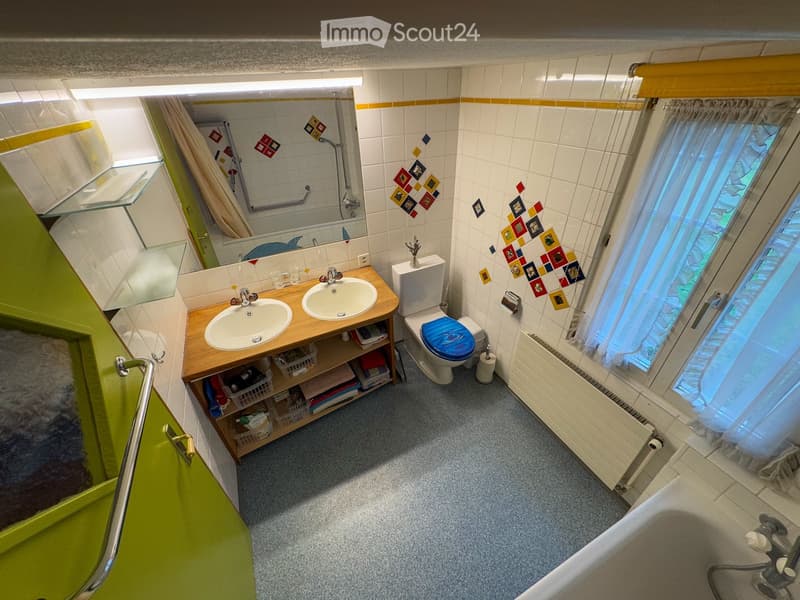 Bathroom with two sinks, toilet, bathtub, shelves, radiator, and colorful tiles.