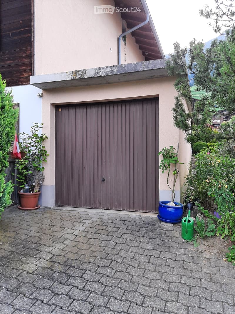 A house with a brown garage door, brick driveway, and potted plants