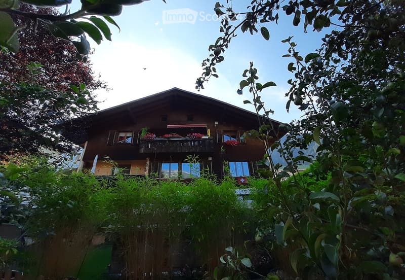 wooden house, 2 stories, balcony, red flowers on balcony, surrounded by trees