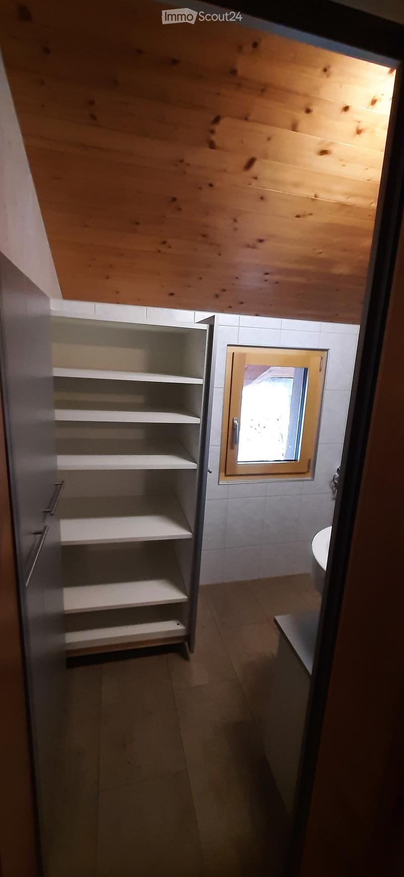 Bathroom with wooden ceiling, white tiled walls, a window, a toilet, and a cabinet with shelves