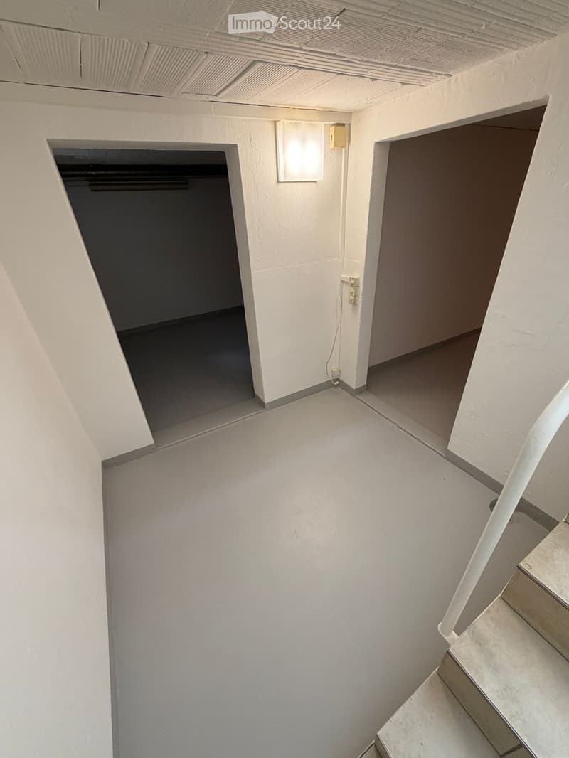 Empty room with two doors, concrete floor, white walls, light on the wall, power outlets, stairs