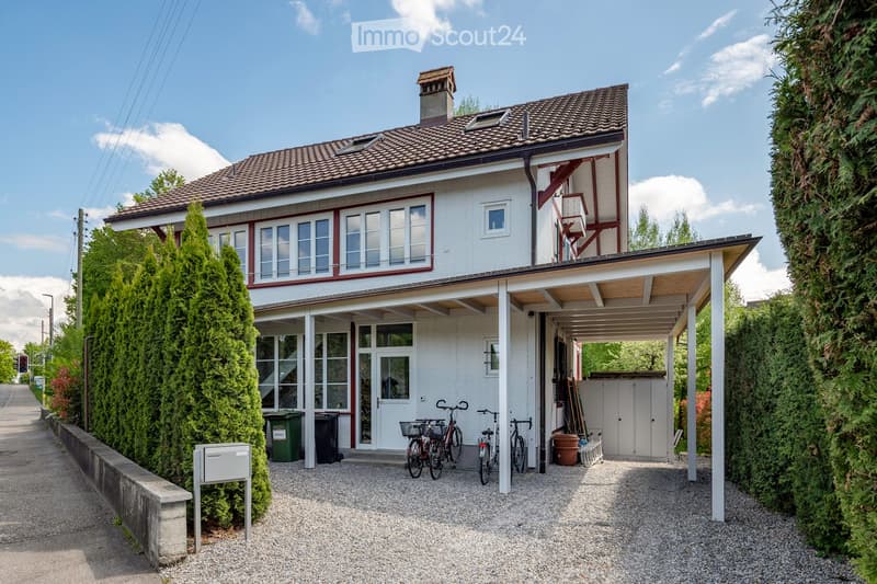 2 story house, white exterior, brown roof, bicycles parked in front, covered carport, trash bins, hedges