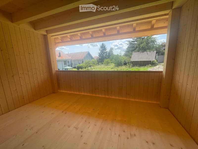 Balcony / Terrace. Empty wooden balcony with open sides, wooden floor, and a view of a rural landscape with houses and trees.