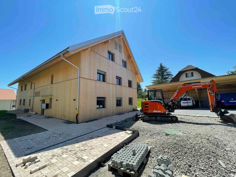 Large wooden house, multiple windows, under construction, excavator in front