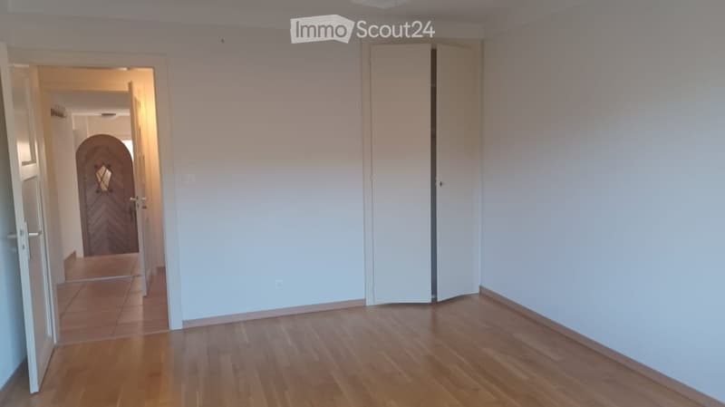 Empty room with wooden floor, white walls, two doors, one leading to another room, closet