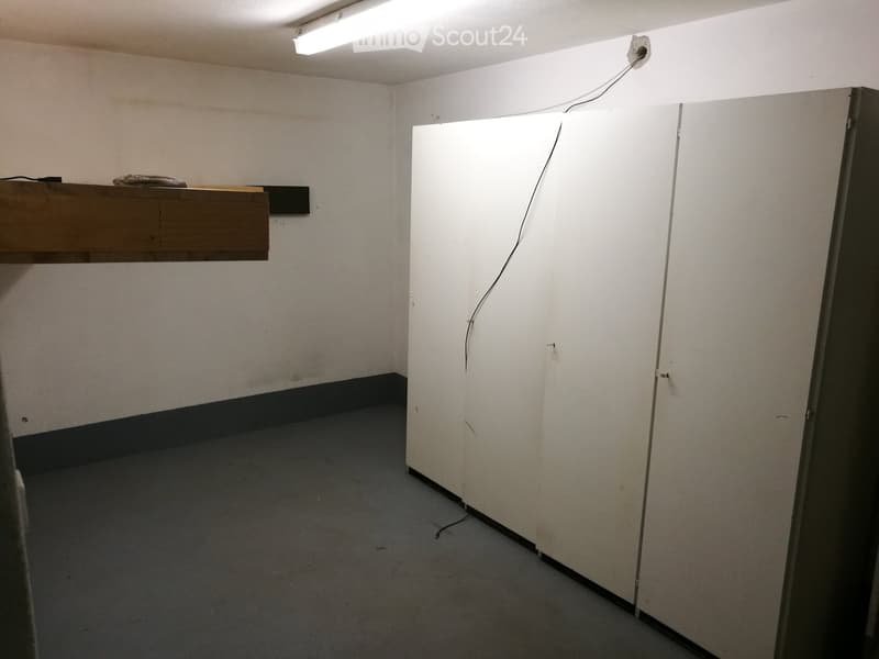 Empty room with white walls, grey carpet, and a wooden shelf on the left side.