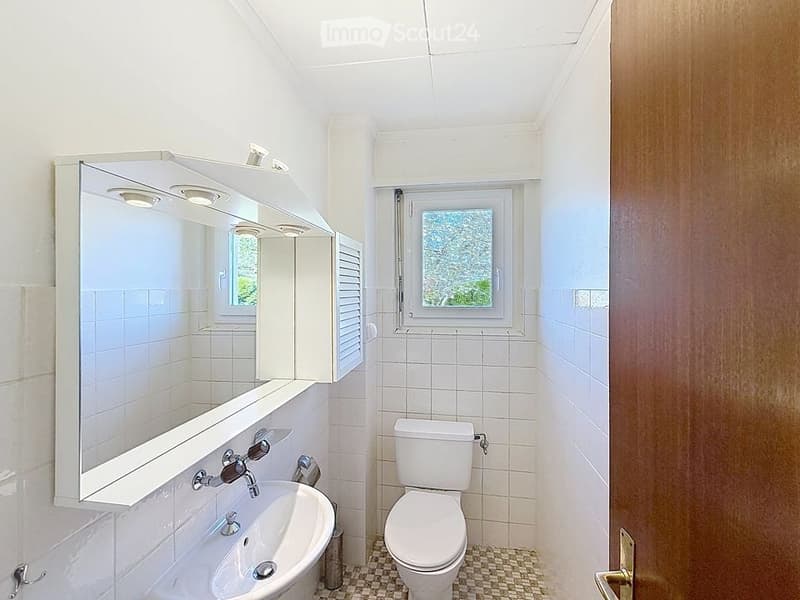 Bathroom with white tiles, white sink, white toilet, mirror, window, wooden door