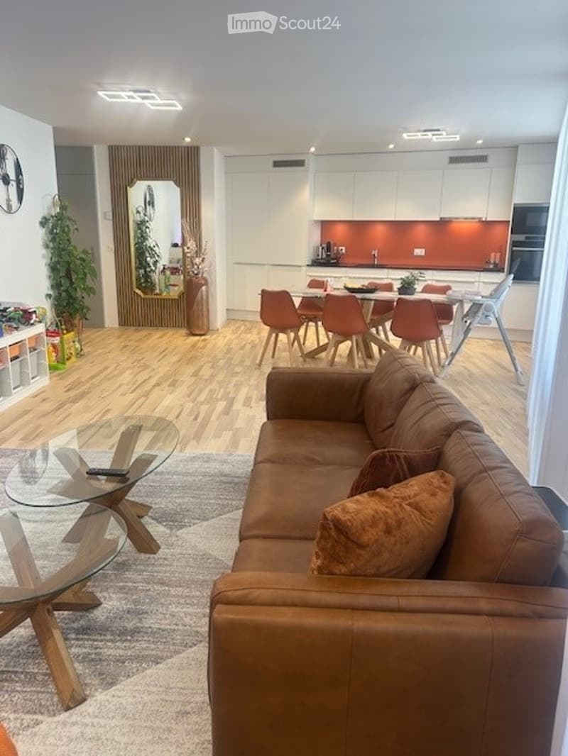 Open-plan living room with a brown leather couch, glass coffee table, and a dining area with chairs around a table.