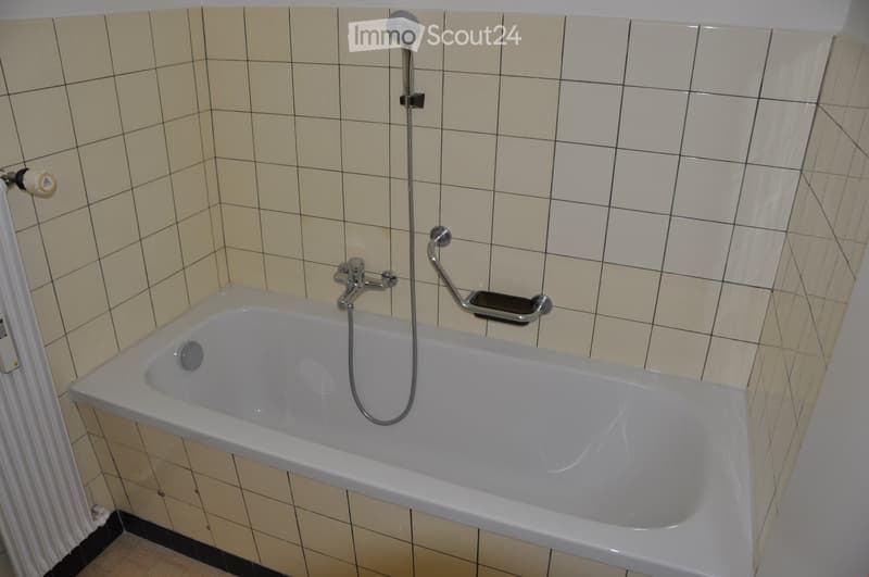 Bathroom with a white bathtub, tiled walls, white shower head, white tiled floor, and white heater