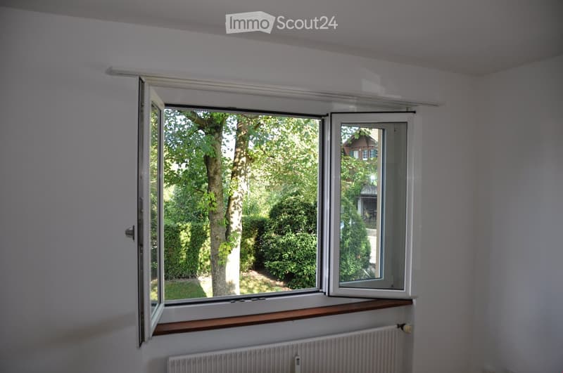 white walls, open window with brown trim, white radiator, grass lawn and trees