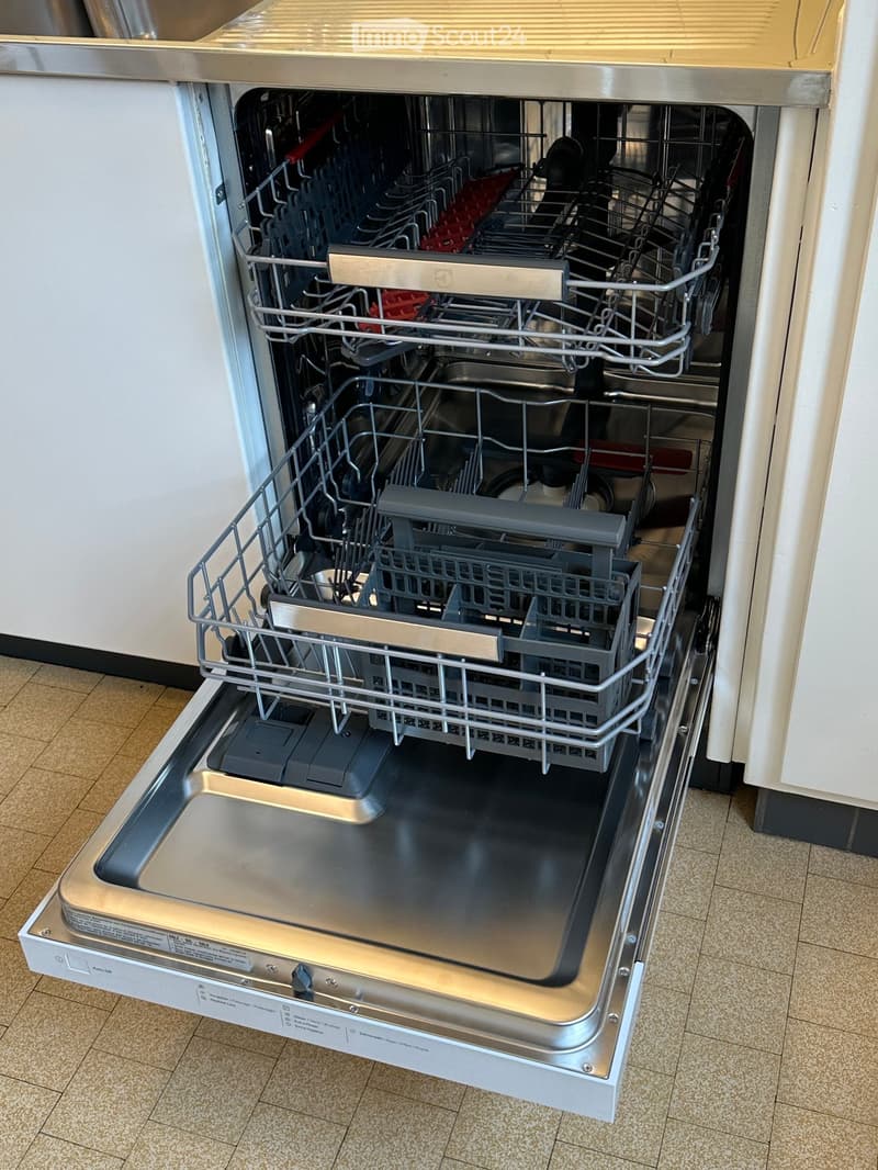Open stainless steel dishwasher, fully loaded with utensils and dishes