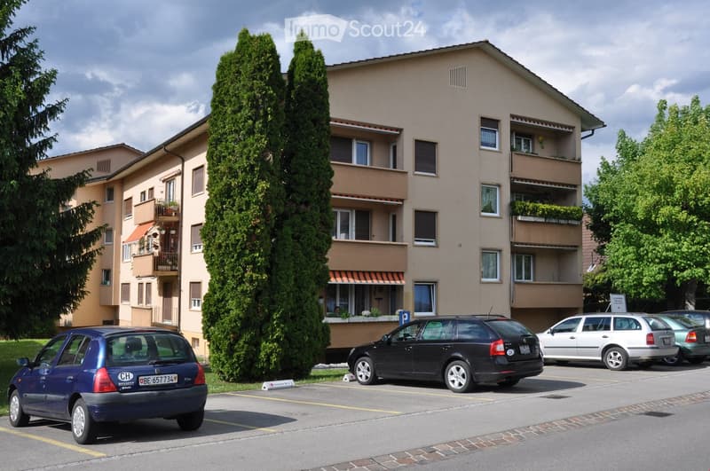 3 story building, multiple balconies, parking area, green surroundings