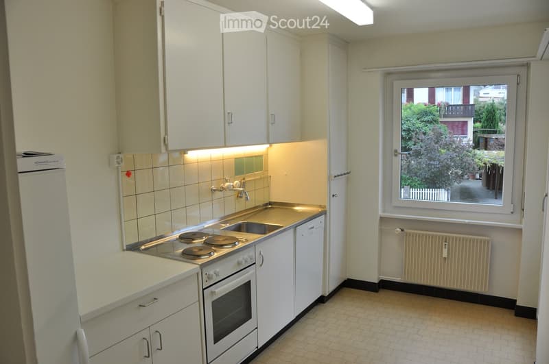 Kitchen. Compact kitchen with white cabinets, a four-burner stove, a sink, and a refrigerator. The space features tiled walls and a window offering a view of greenery outside.