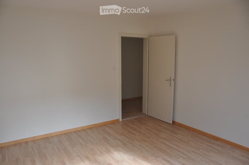 Unfurnished Room. Empty room with light-colored walls and wooden flooring, featuring an open doorway leading to another room.