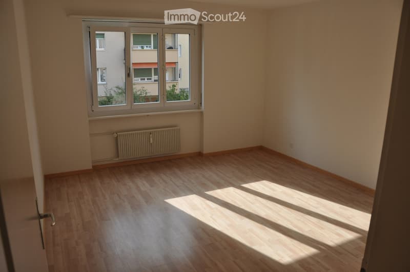 Unfurnished Room. Empty room with wooden flooring, large window, radiator, and natural light streaming in.