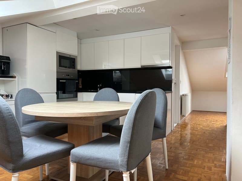Kitchen. Modern kitchen with white cabinets, a round wooden dining table, four grey upholstered chairs, and built-in appliances including a microwave and oven.