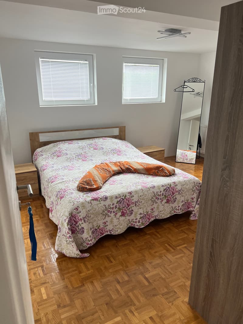 Bedroom. Bedroom with wooden flooring, a bed with floral bedding, a nightstand, a mirror, and a wardrobe.