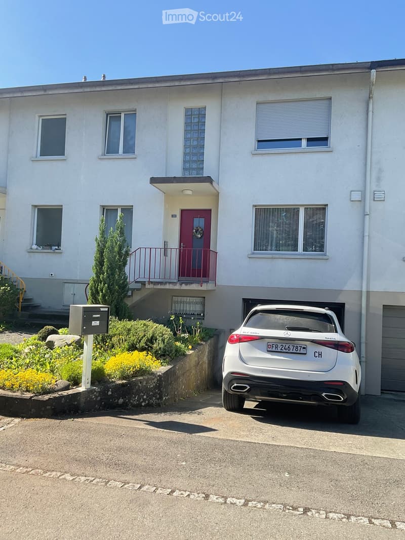 Two-story house with white exterior, red front door, balcony, and a white car parked in the driveway.
