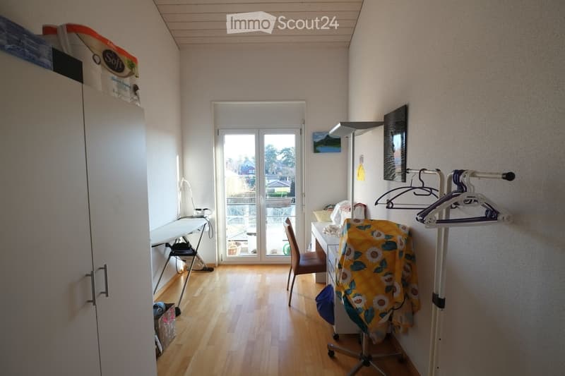A room with a desk, chair, ironing board, storage boxes, and a coat rack.