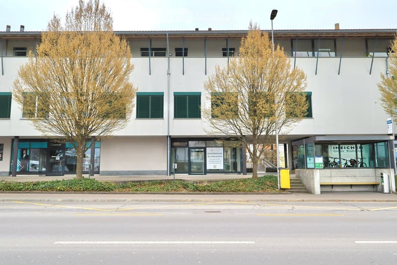 A white building with green shutters and glass doors, bicycles parked in front, and a streetlight on the right.
