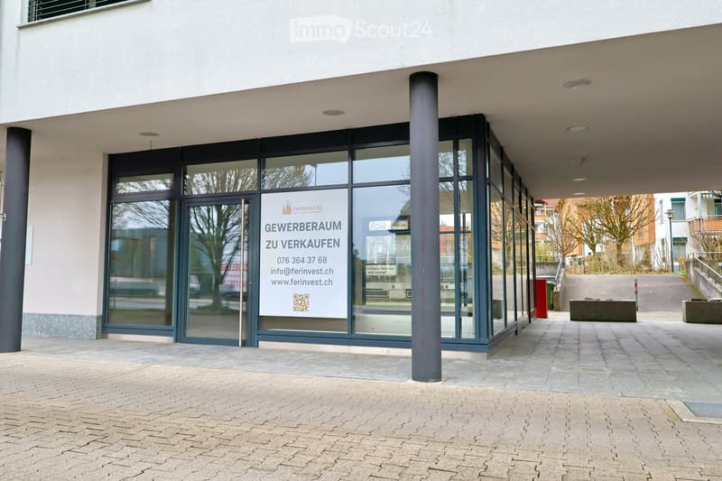 Exterior of a modern building with glass doors and windows, a sign indicating commercial space for sale.