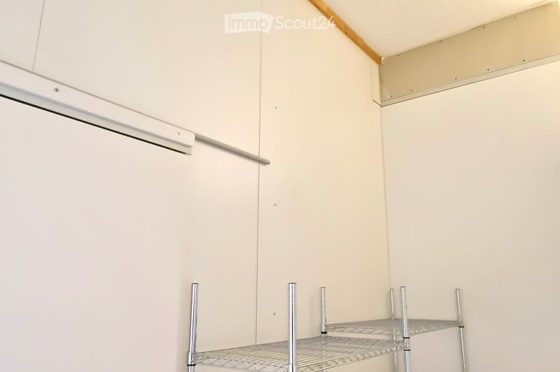 An empty room with white walls, ceiling, and floor. There is a metal shelving unit against the wall and a white door with a silver handle.