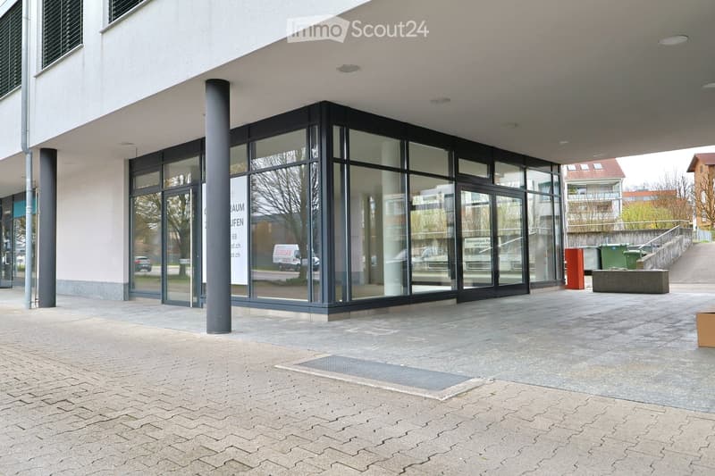 Modern building with glass facade, large entrance, and a signboard. The entrance has glass doors and windows, and the building has a brick wall and a metal railing.