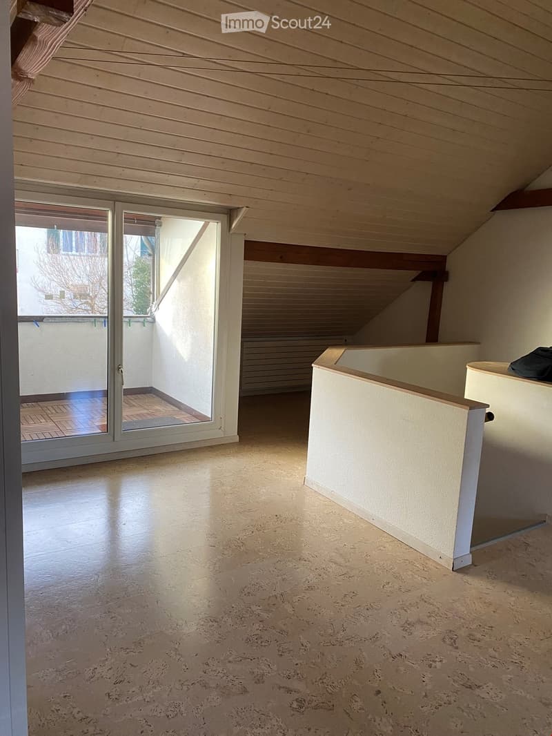 spacious attic room, white walls, hardwood floor, sliding glass doors leading to balcony, wooden ceiling