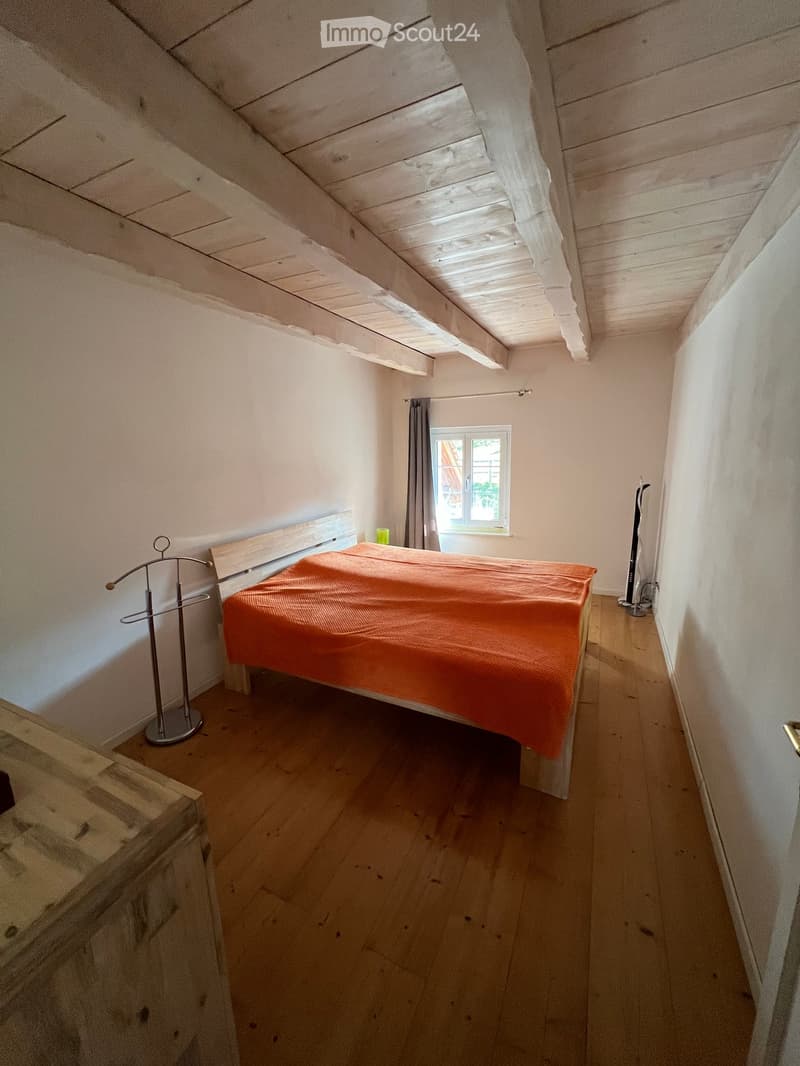 Cozy attic bedroom with wooden floors, slanted wooden ceiling, skylight window, and a single bed with orange bedding.