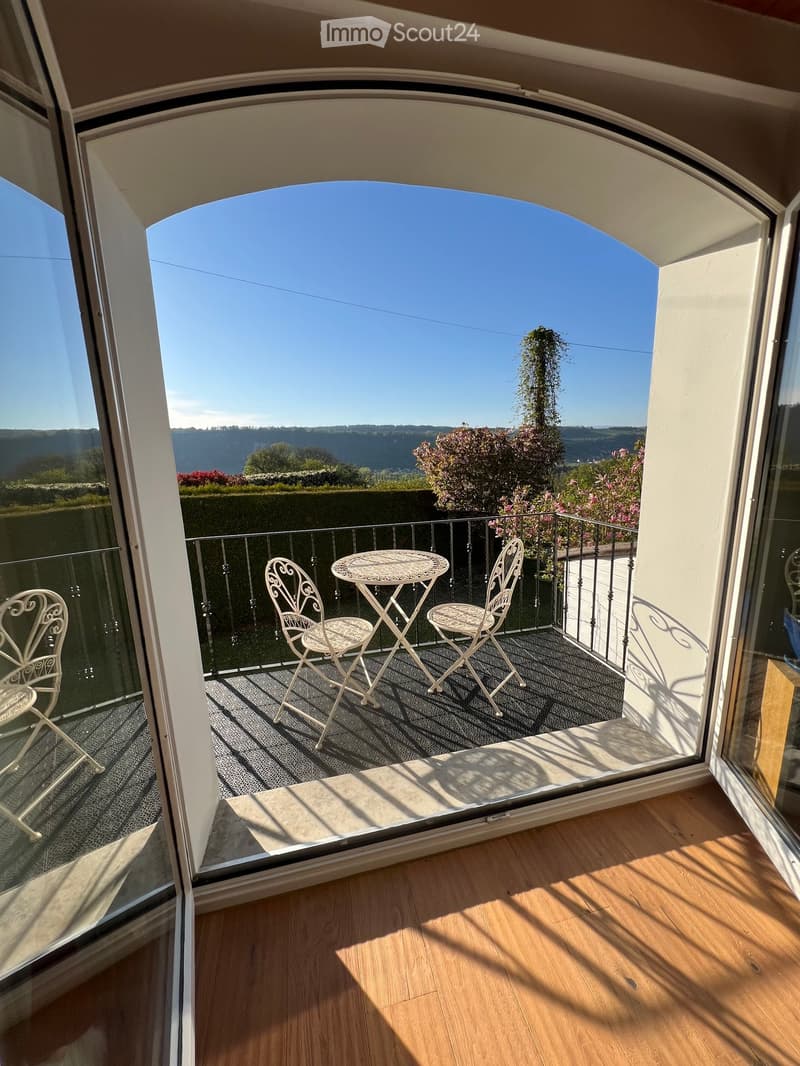 Balcony with a table and chairs, overlooking a scenic valley view with trees and hills.