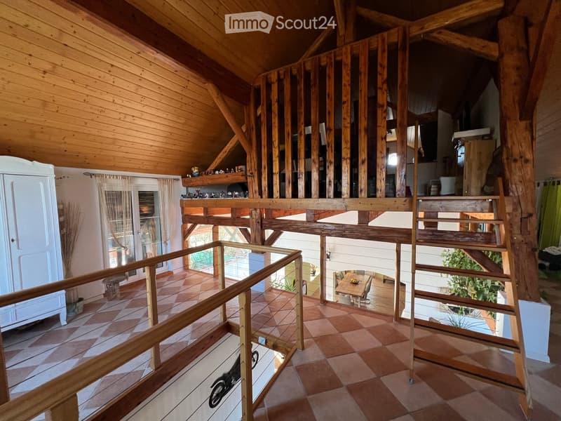 Spacious, open-concept house with wooden beams, exposed wooden ceiling, and a multi-level layout. Features include a tiled floor, a staircase leading to an upper level, and a balcony overlooking the living area.