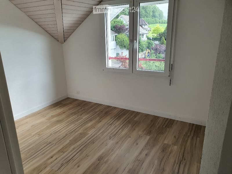 Unfurnished Room. Empty room with wooden floor and white walls. There is a window with a view of a house and garden outside.