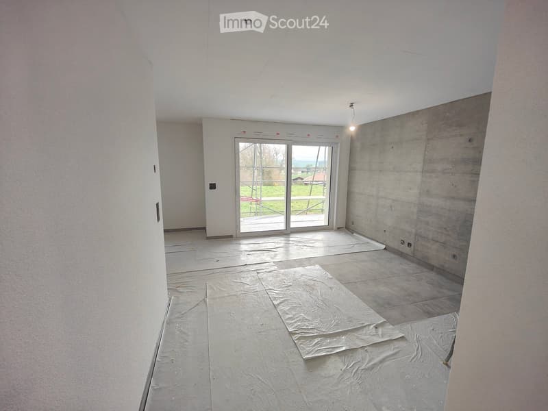 Empty room with white walls, white floor, sliding glass door, concrete wall, and a view of the outside.