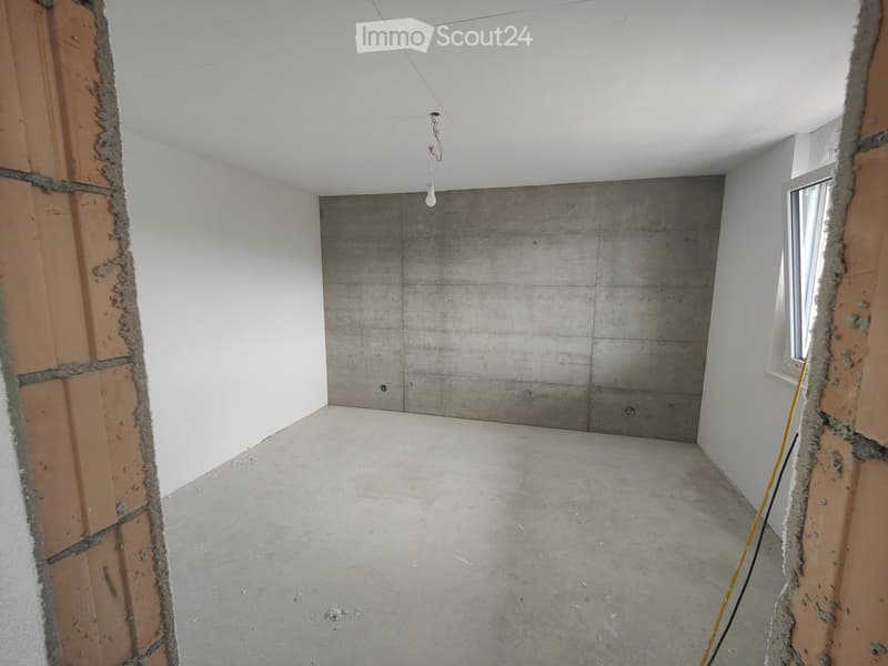 Empty room with concrete wall, white walls, concrete floor, window, and a light fixture