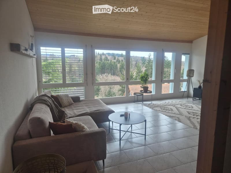 living room with large windows, couch, coffee table, rug, wooden ceiling, view of the forest