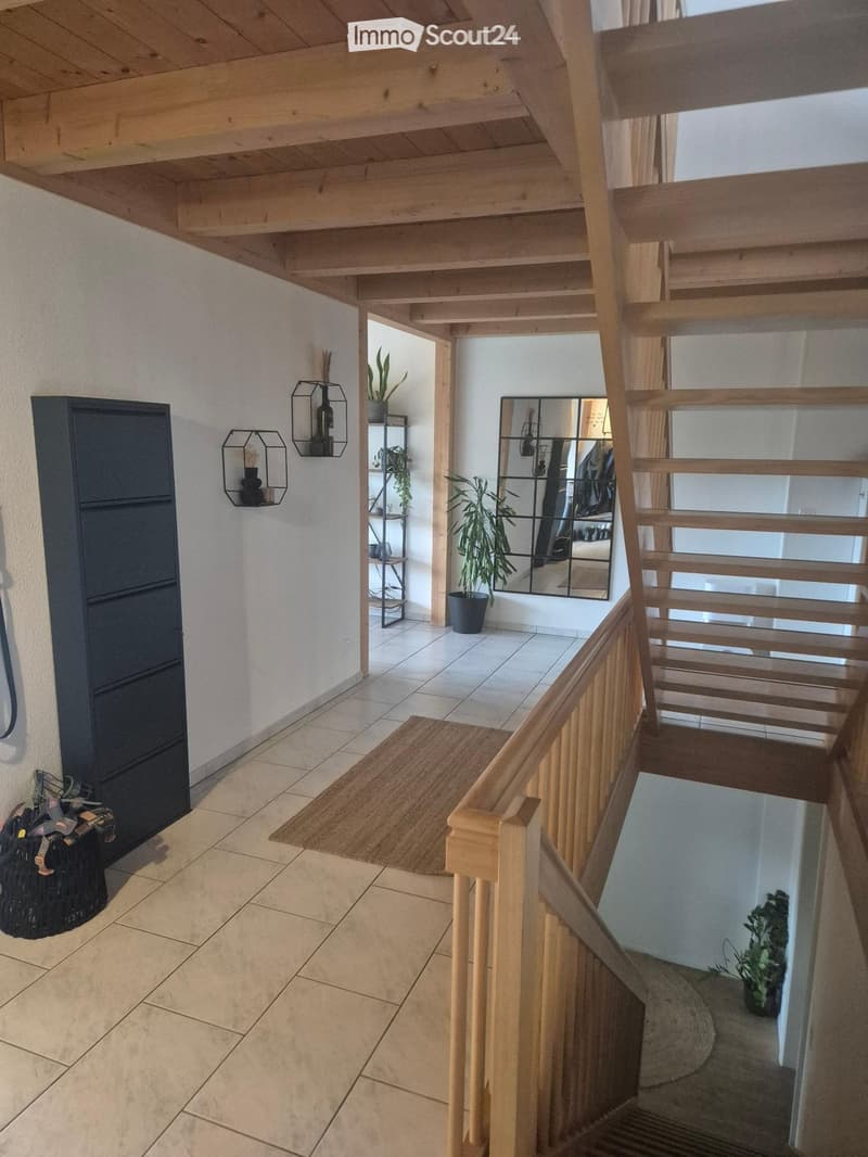 Entrance hall with wooden ceiling, tiled floor, wooden staircase, storage cabinet, mirror, plants, rug