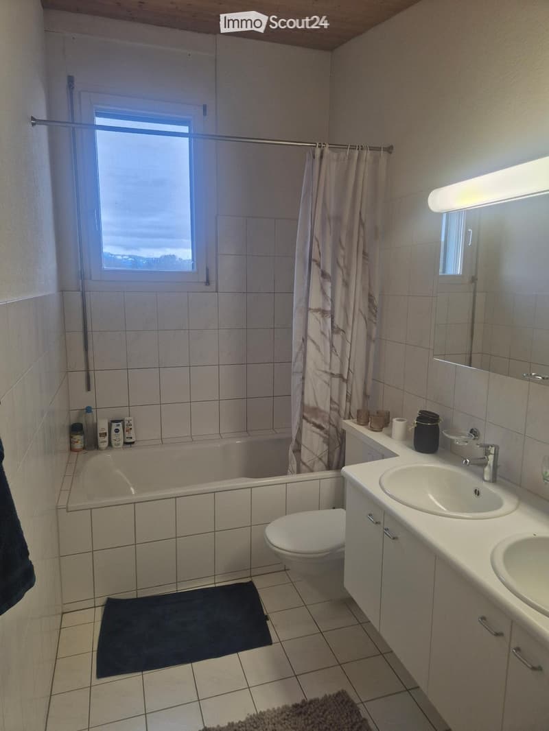 Bathroom with white tiles, bathtub, toilet, two sinks, mirror, and a window