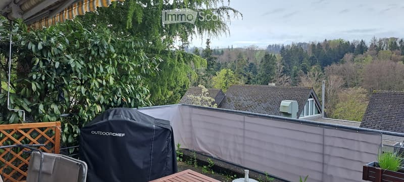 Balcony with wooden fence, covered with awning, covered grill, outdoor chef cover, wooden table, chair, plants, and a view of the surrounding area