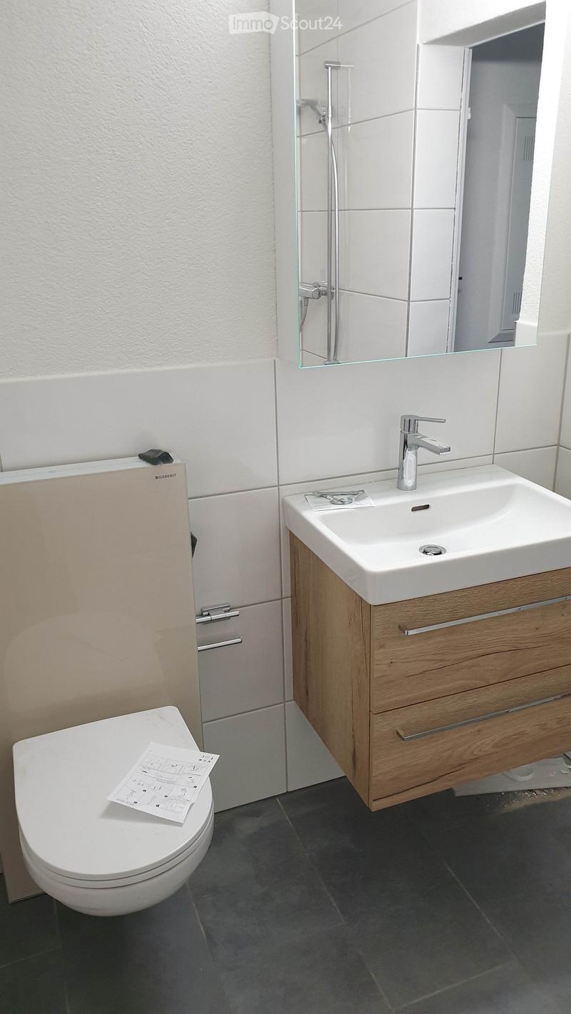 Bathroom with white tiles, a toilet, a sink, a mirror, and a wooden cabinet.