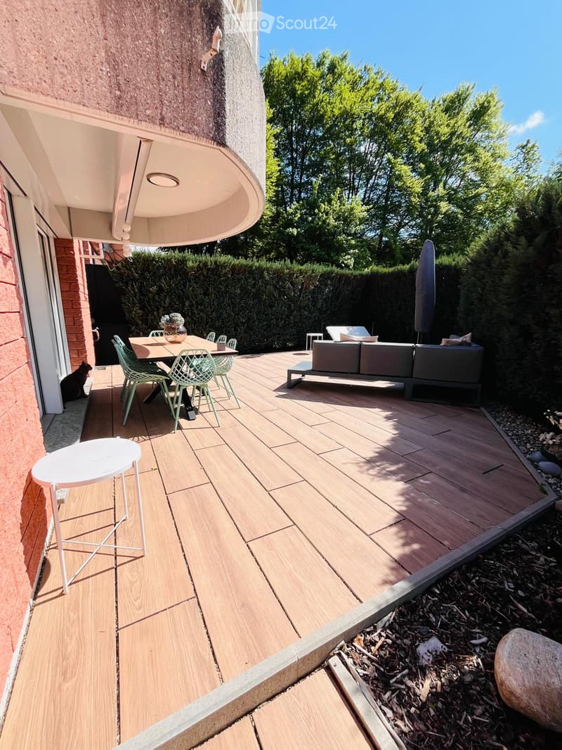 Outdoor area with wooden deck, table, chairs, couch, and umbrella. A vase with flowers on the table.