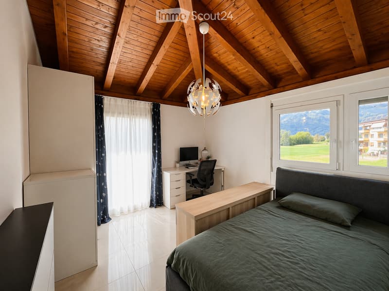 A bedroom with a bed, desk, chair, computer monitor, lamp, nightstand, wardrobe, cabinet, pillow, and vase.