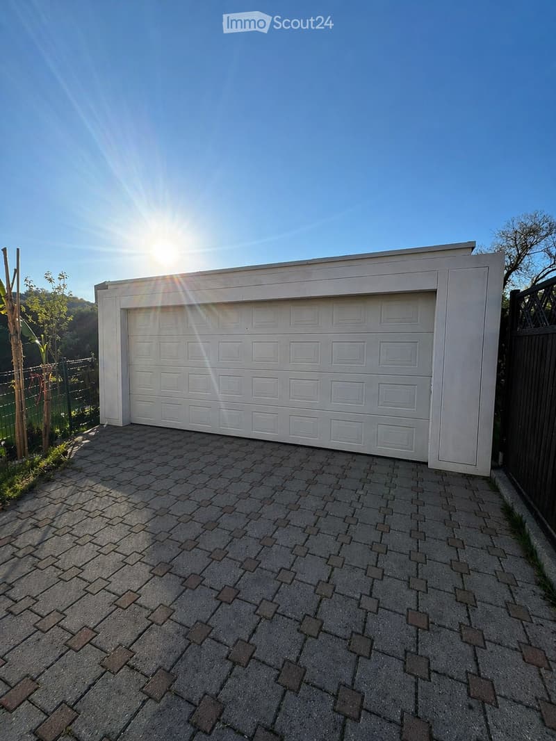 A white garage with a brick driveway, a closed garage door, and a black fence on the side.