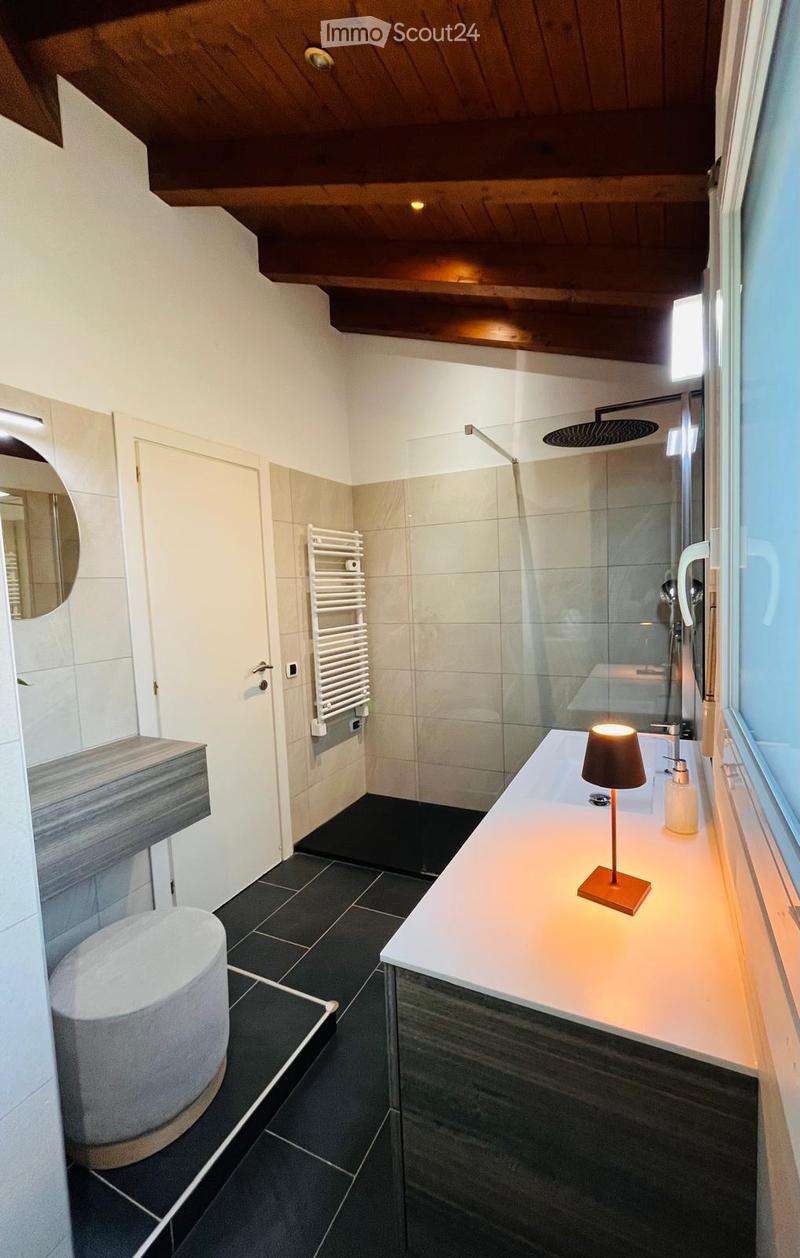 Modern bathroom with white tiles, a glass shower enclosure, a white sink, and a round ottoman.
