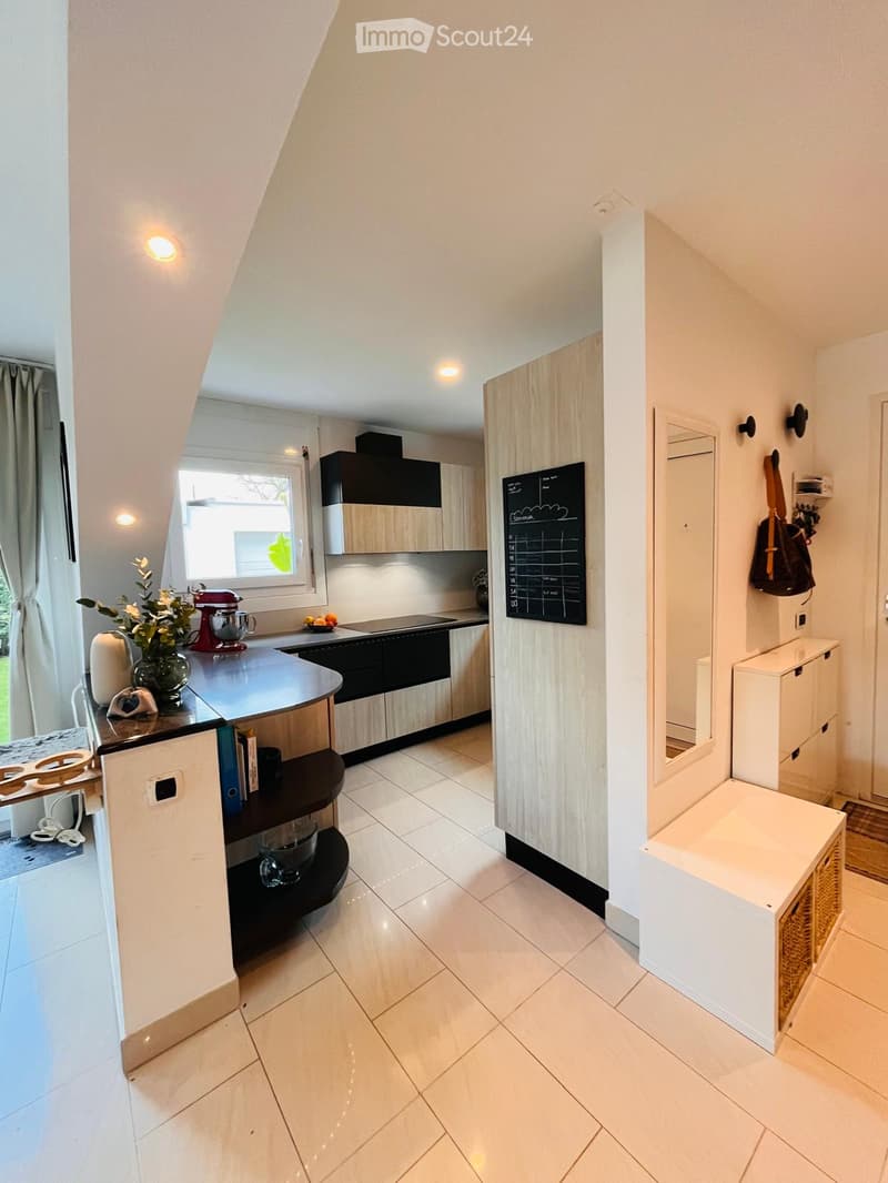 Modern kitchen with white tiled floor, black and white cabinets, a central island, and a blackboard. A mixer, flowers, and books are on the island. A mirror and a handbag are on the wall.