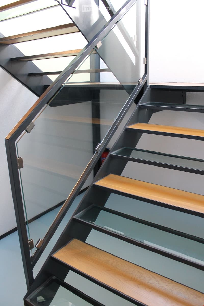 Corridor / Hallway. Modern staircase with glass steps and wooden treads, black metal handrail, and glass panels.